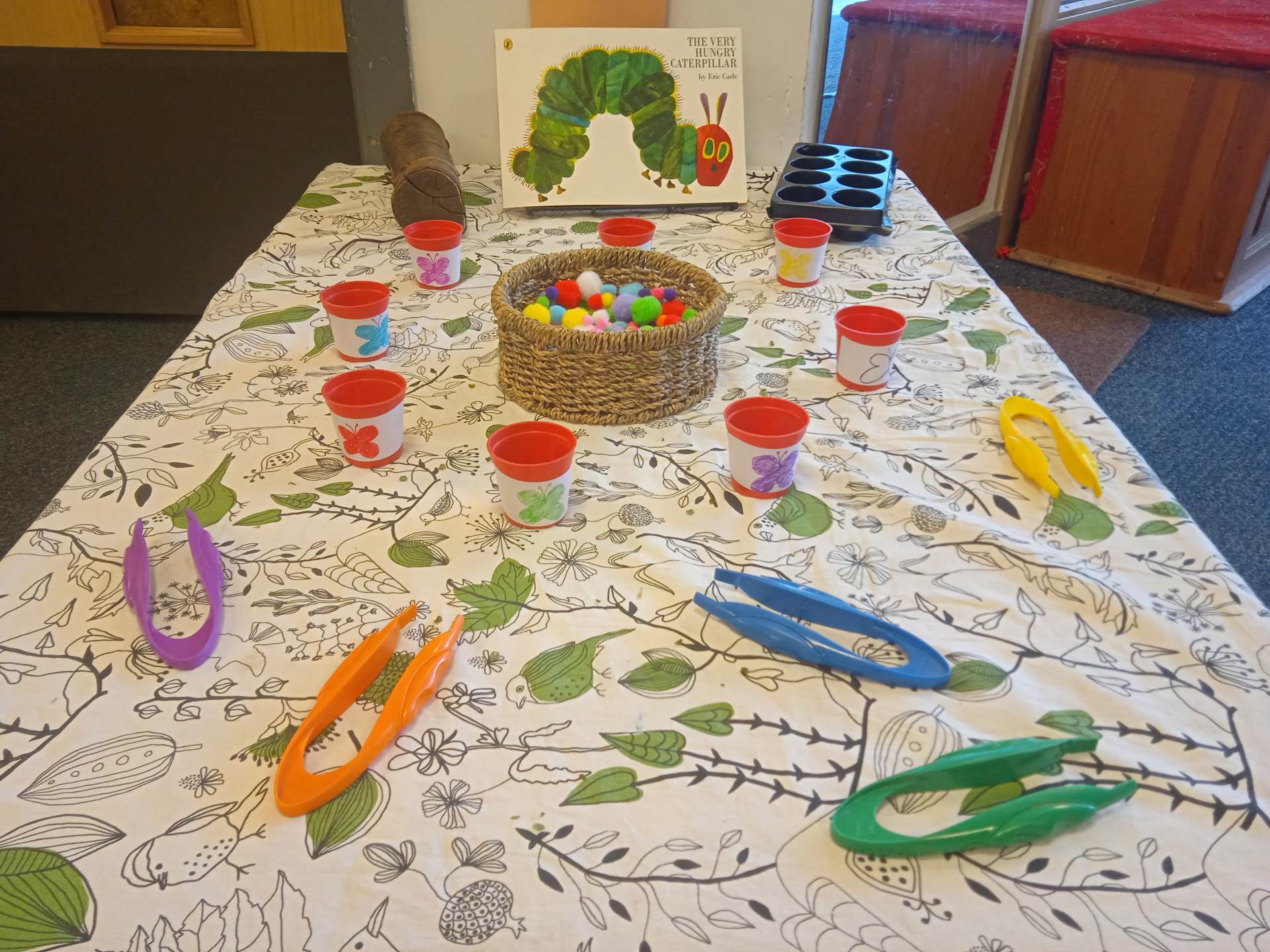 Basket of pompoms with large tweezers and small plantpots